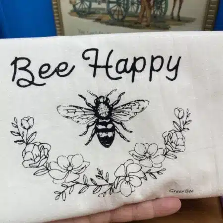 cotton tea towel with a floral garland and a bee centered that says " bee happy" slightly flawed kitchen tea towel