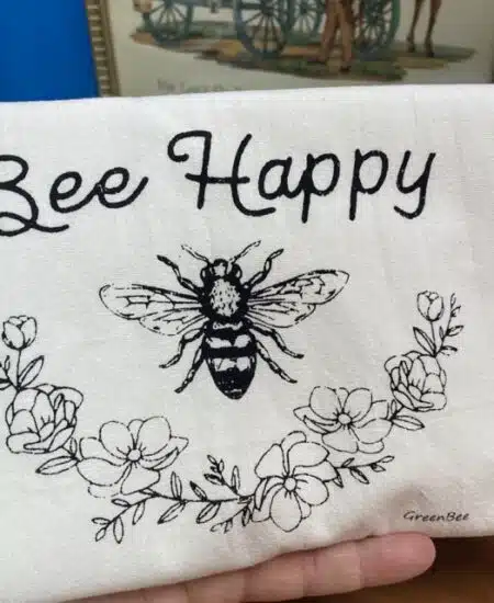 cotton tea towel with a floral garland and a bee centered that says " bee happy"