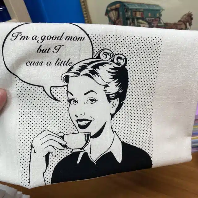 tea towel that shows a women drinking out of a tea cup that says "I'm a good mom, but I cuss a little: